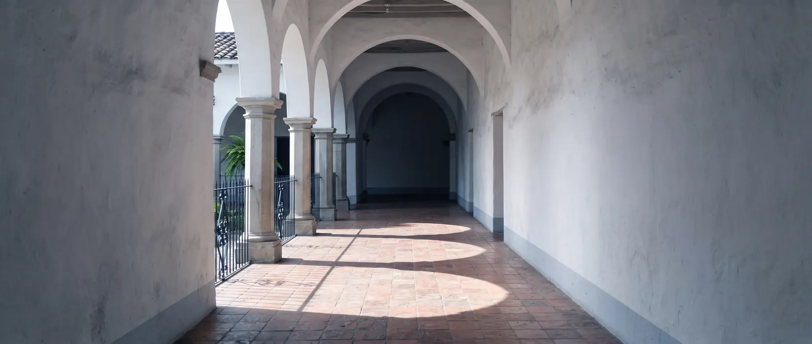 Morning light falling through the arches of an empty colonial corridor.