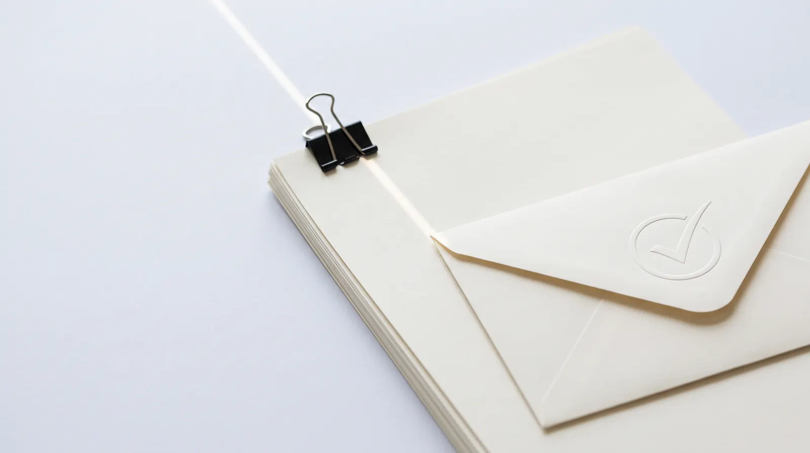 A clipped stack of documents beside an envelope embossed with a ring and a check mark.